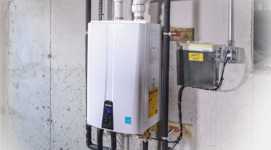 White tankless water heater installed on a cement basement wall.