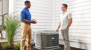 HVAC technician and homeowner stand beside an outside air conditioning unit, talking.