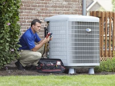 Technician inspecting outdoor HVAC unit beside brick home.